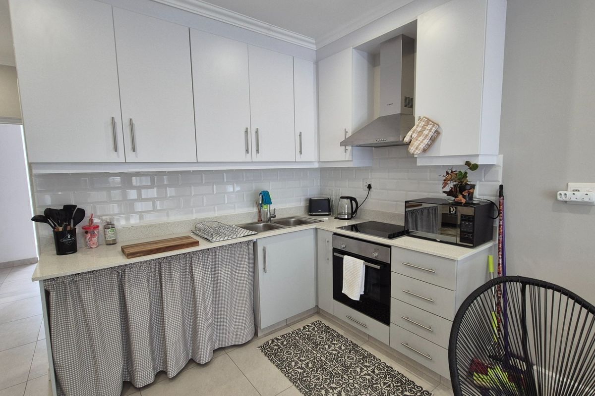 A functional kitchen featuring white cabinetry, subway tile backsplash, stone countertops, and integrated stainless steel appliances including an oven and extractor fan.