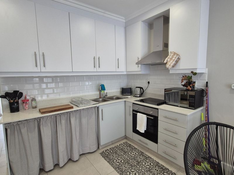 A functional kitchen featuring white cabinetry, subway tile backsplash, stone countertops, and integrated stainless steel appliances including an oven and extractor fan.