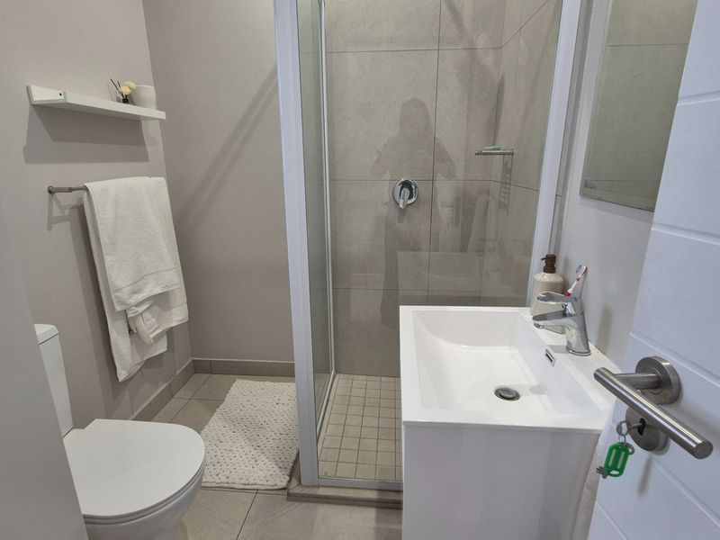 A modern, well-maintained bathroom featuring a glass-enclosed shower, a sleek vanity basin with mixer tap, and neutral wall and floor tiling.