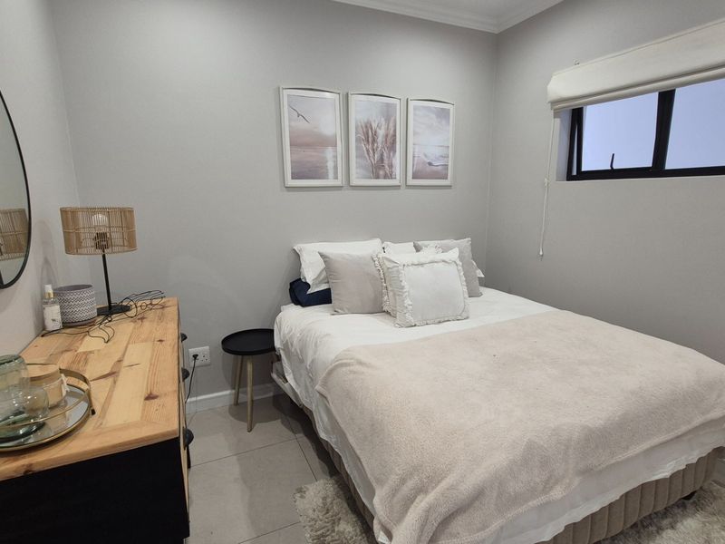 A well-maintained bedroom featuring neutral wall tones, tiled flooring, and a functional window with a roller blind.