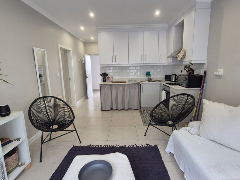 An open-plan living area featuring a compact kitchen with white cabinetry, subway tile backsplash, and modern recessed lighting throughout the space.