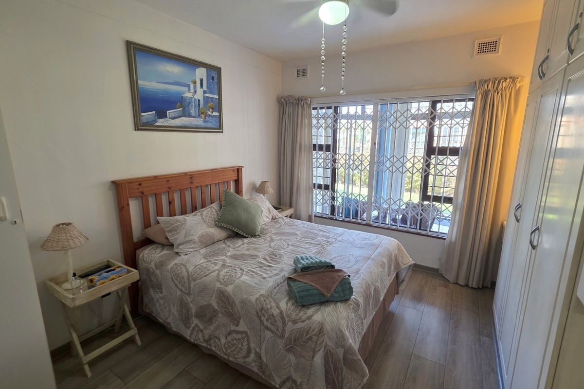 A well-lit bedroom featuring built-in wardrobes, wood-look flooring, and a security gate over the window.