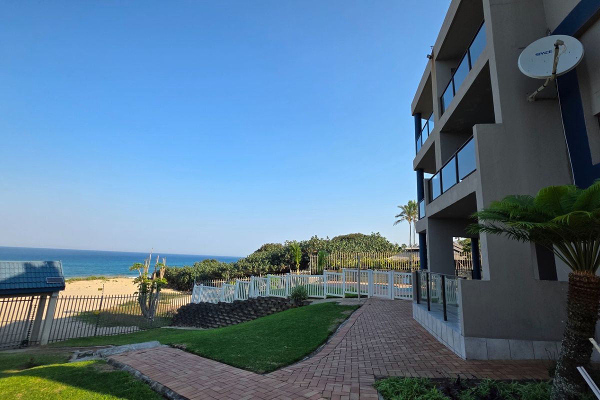 Exterior view of the apartment building featuring paved walkways, landscaped garden areas, and direct access to the beach and ocean.