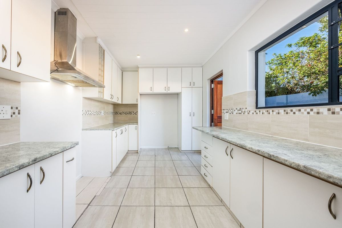 A clean, functional kitchen featuring white cabinetry, granite-look countertops, tiled backsplash, stainless steel extractor fan, and neutral floor tiles.