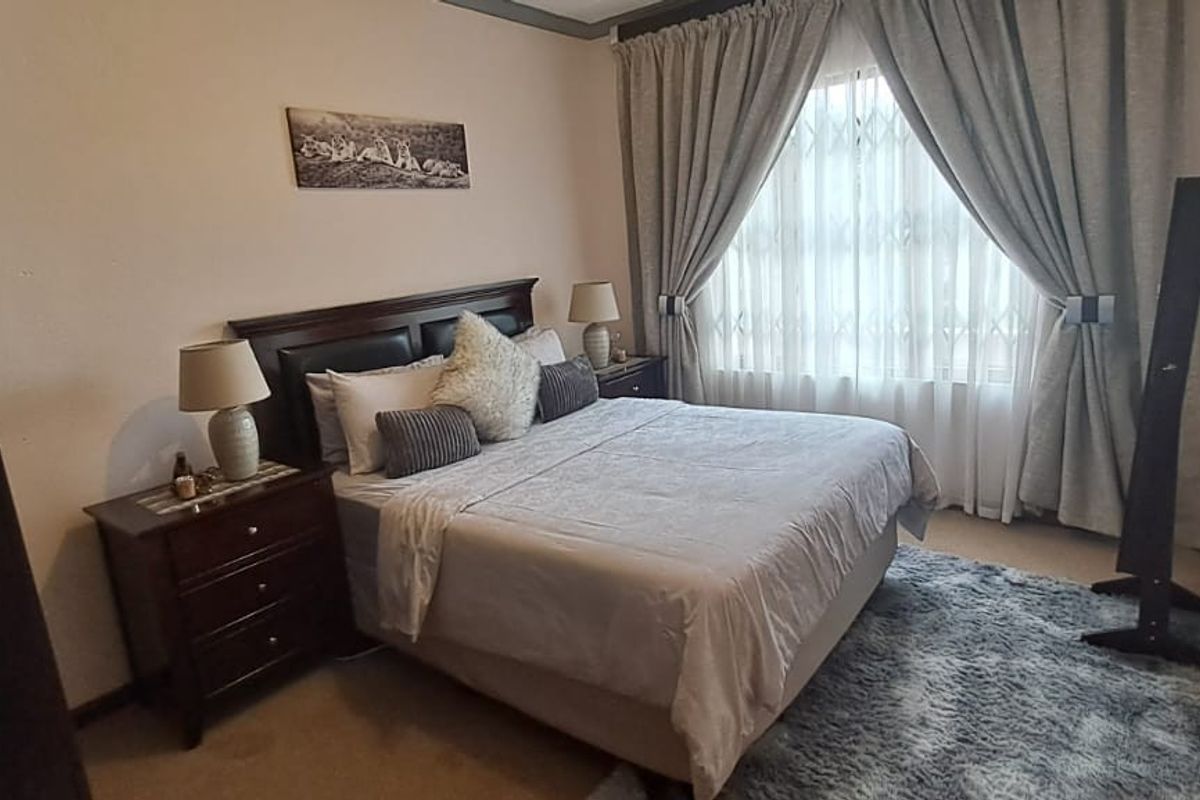 A standard bedroom featuring neutral wall finishes, carpeted flooring, and a window fitted with a security gate and curtains.