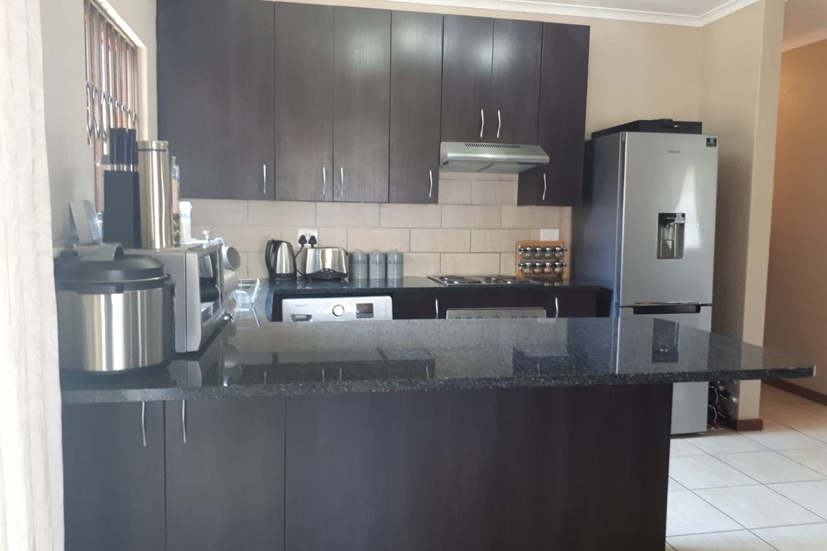A functional kitchen featuring dark wood cabinetry, granite countertops, a tiled backsplash, and built-in cooking appliances with a breakfast bar peninsula.