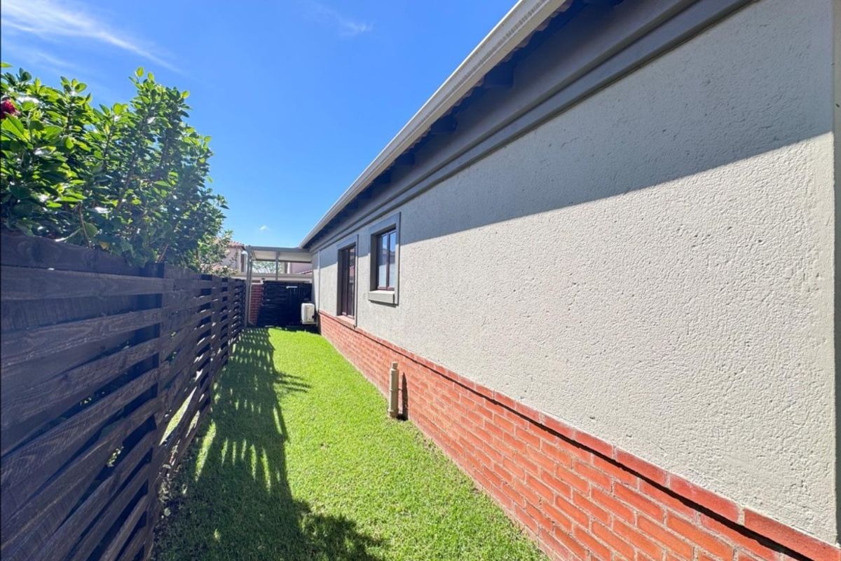 A well-maintained side garden area featuring a neat lawn, timber fencing, and a clean brick and plaster exterior wall finish.
