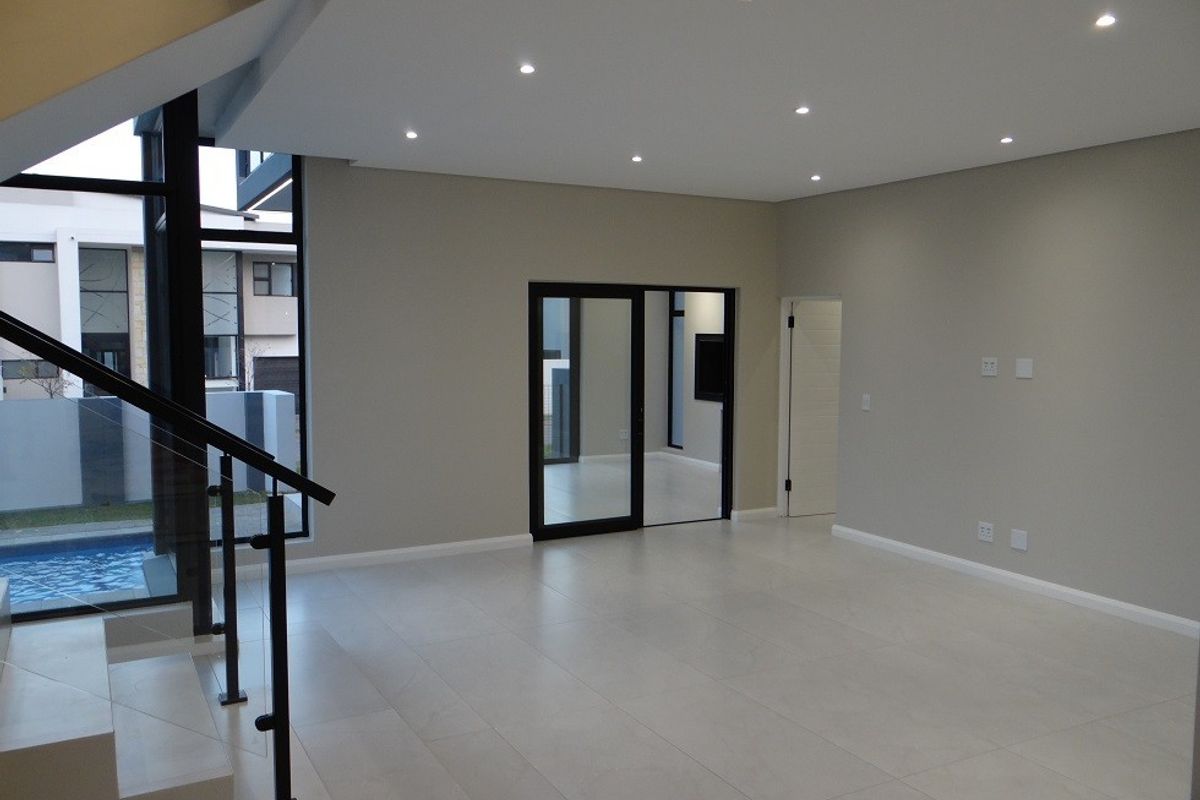Spacious, modern open-plan living area featuring neutral tiled floors, recessed lighting, and a contemporary staircase with glass balustrades overlooking the pool area.