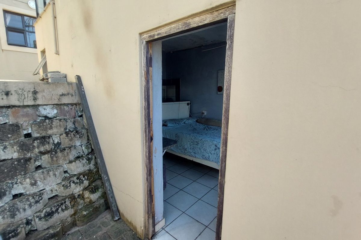An exterior view of a doorway leading into a bedroom, showing signs of significant wear and maintenance requirements on the building facade.