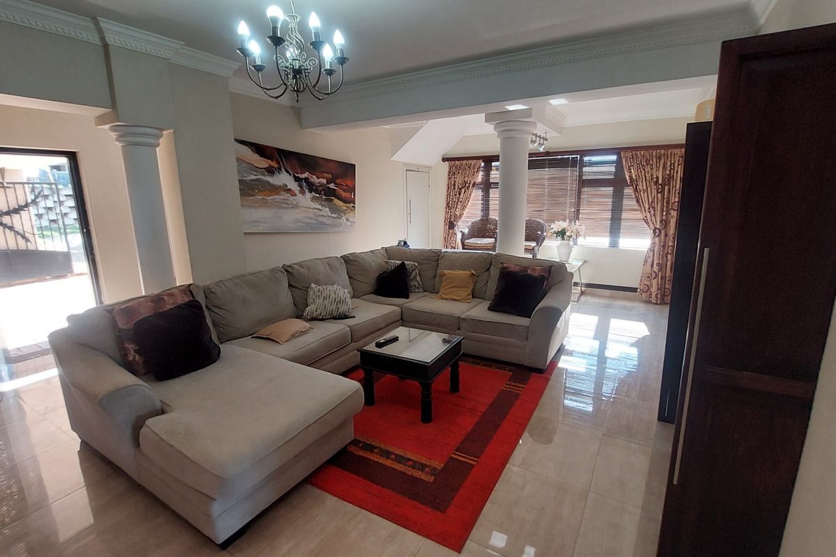Spacious living room featuring tiled flooring, decorative columns, crown molding, and a classic chandelier, offering a bright and open atmosphere.