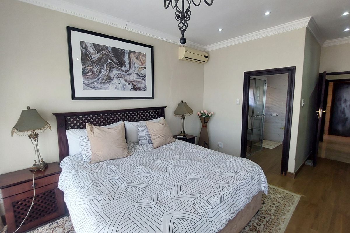 Spacious bedroom featuring crown molding, recessed lighting, a wall-mounted air conditioning unit, and an en-suite bathroom with a glass shower enclosure.