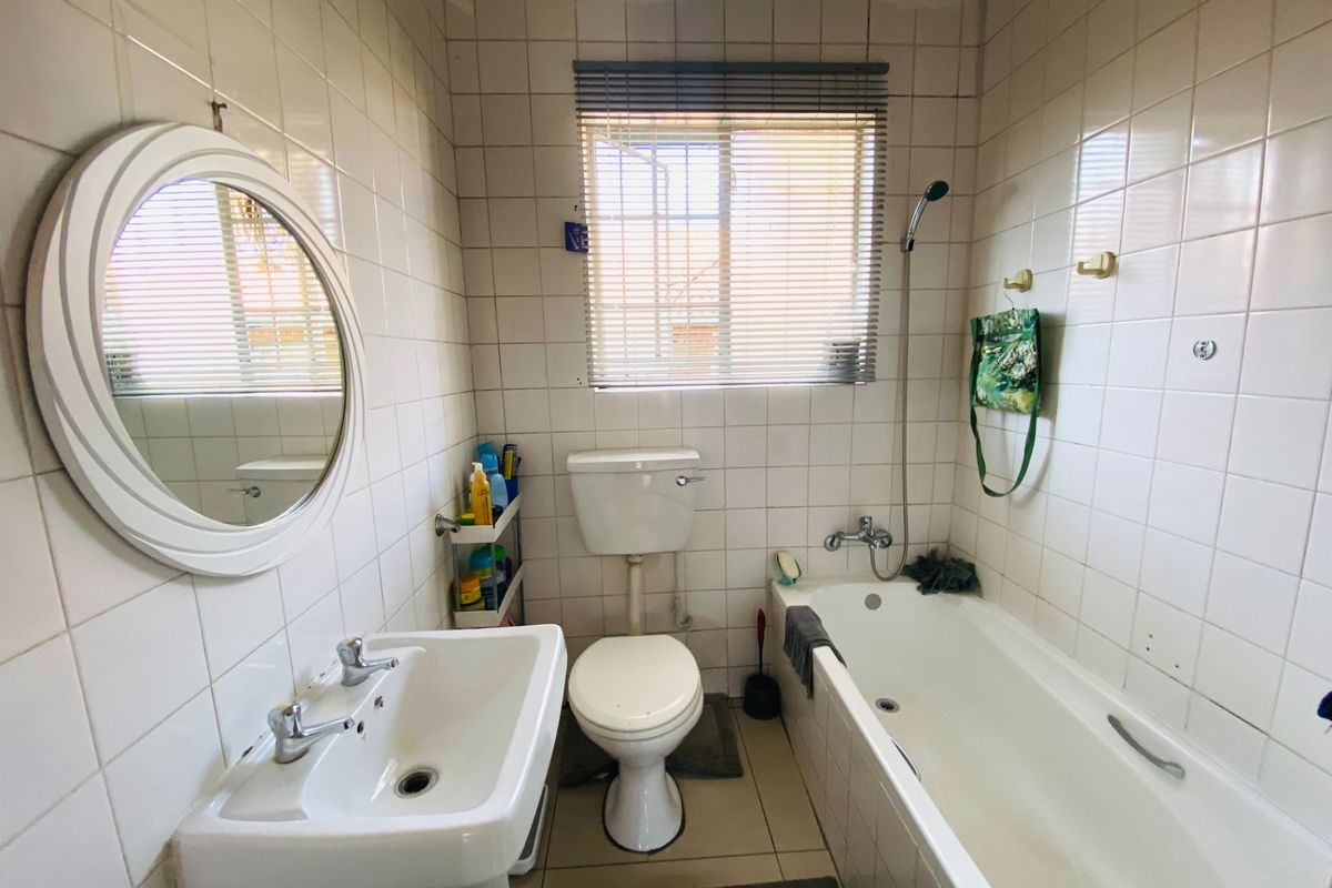 A functional bathroom featuring a standard bathtub with shower mixer, pedestal basin, and toilet, finished with full-height wall tiling and a window.