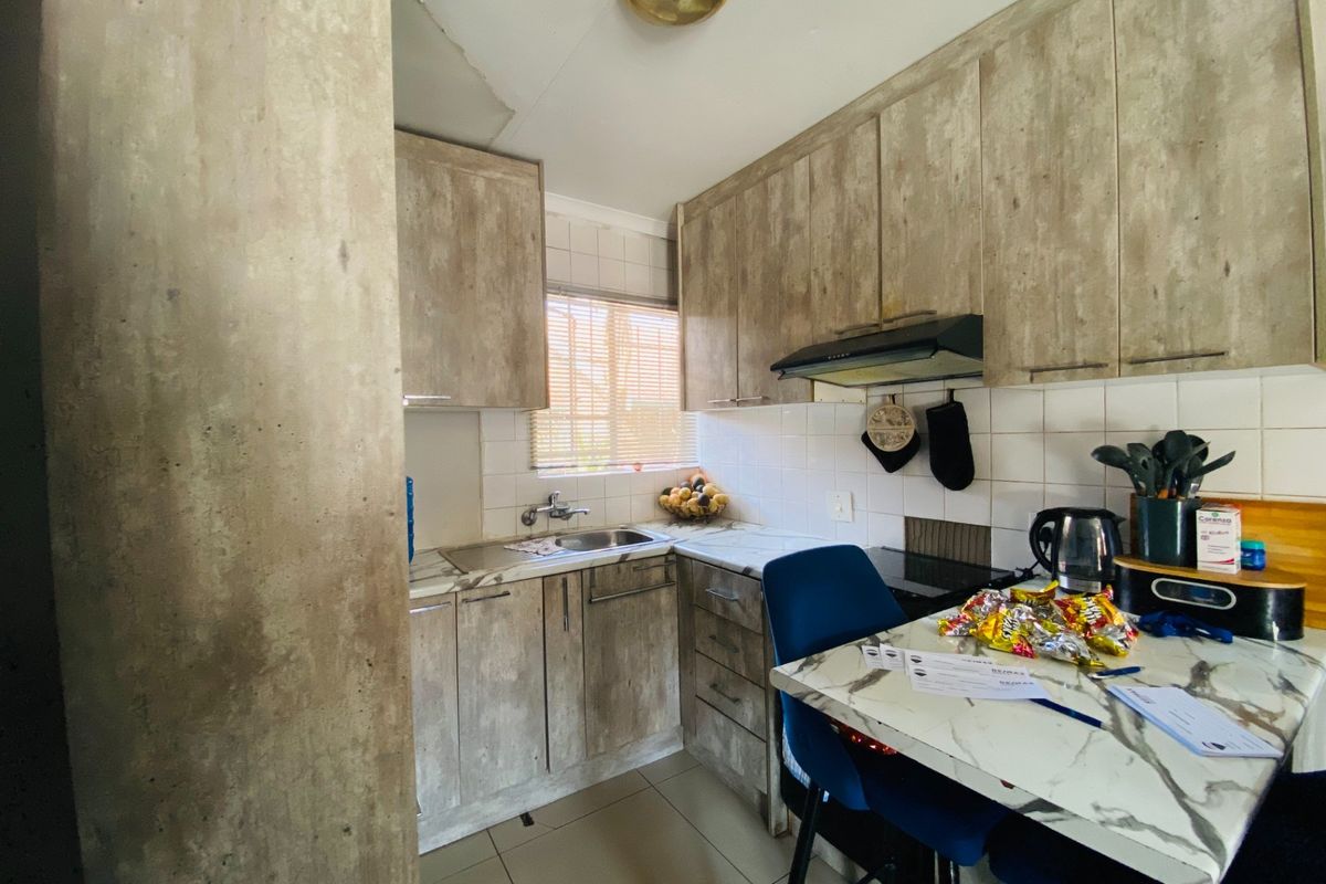 Compact kitchen featuring wood-look cabinetry, tiled backsplash, built-in extractor fan, and a small breakfast nook area.