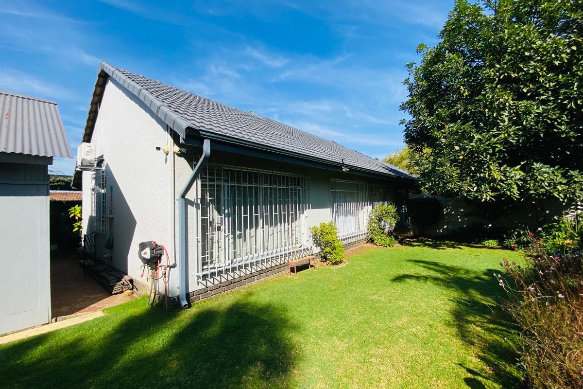 Rear view of the house featuring a tiled roof, security bars on windows, and a well-maintained lawn area.