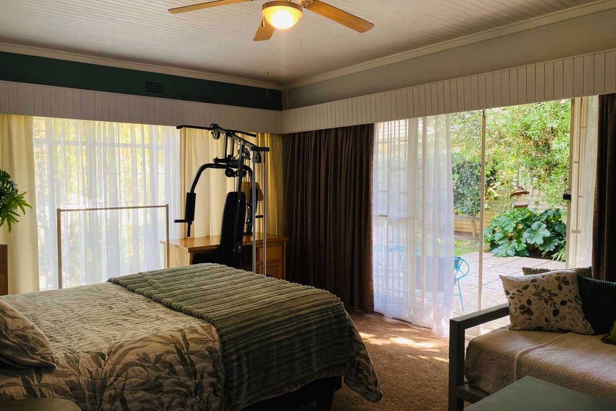Spacious bedroom featuring a ceiling fan, carpeted flooring, and large sliding glass doors providing direct access to the rear patio and garden area.