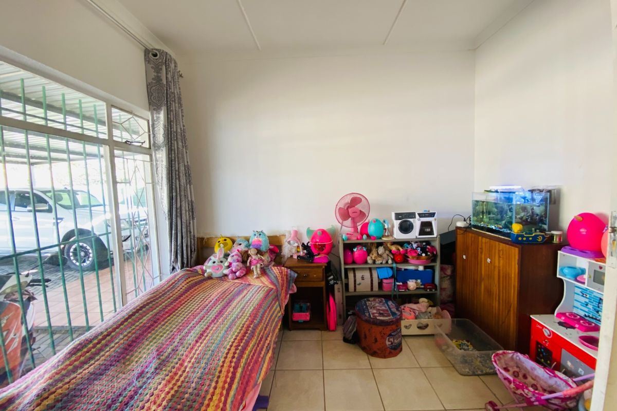 A bedroom featuring tiled flooring, large sliding glass doors with security bars, and direct access to the exterior driveway area.