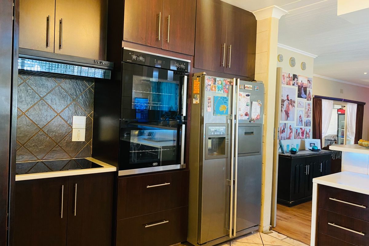 A functional kitchen featuring dark wood cabinetry, a built-in double oven, a glass cooktop, and a tiled backsplash, leading into an adjacent living area.