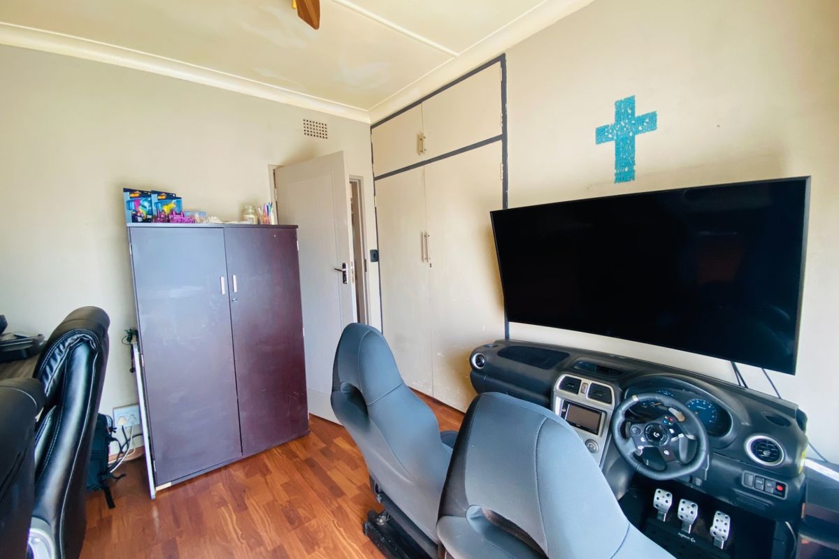 A bedroom featuring built-in cupboards, laminate flooring, and a ceiling fan, currently utilized as a gaming and office space.