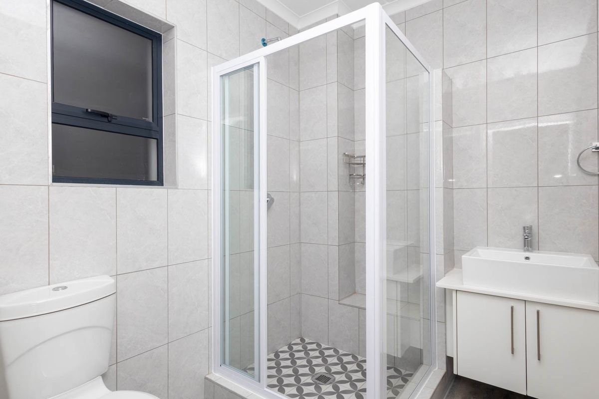 Modern bathroom featuring a glass-enclosed shower with patterned floor tiles, a white vanity with a vessel sink, and a dual-flush toilet.