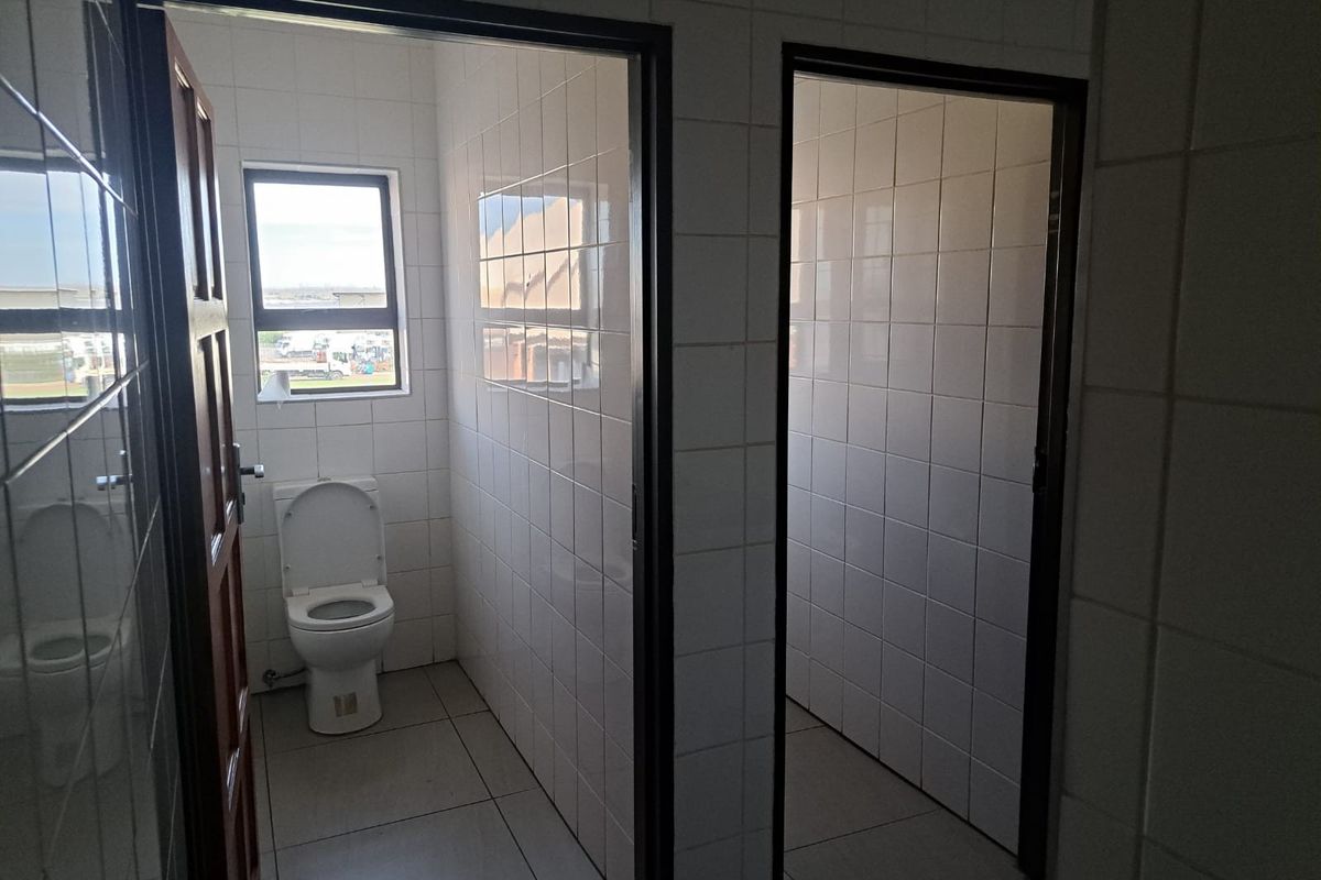 Functional industrial restroom facility featuring tiled walls and floors, including a private toilet cubicle with natural light.