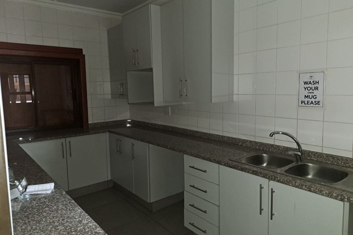 A functional kitchen area featuring light-toned cabinetry, granite-look countertops, a double-basin stainless steel sink, and tiled wall splashbacks.