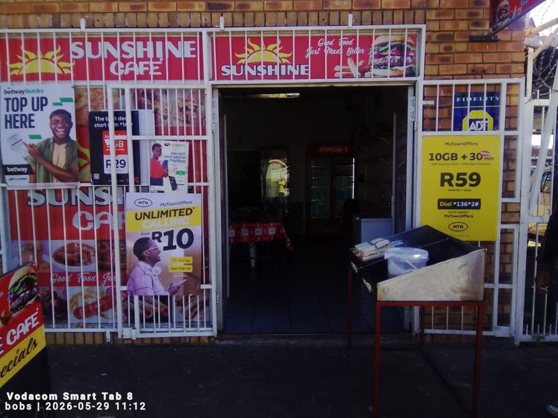Front entrance of a commercial cafe featuring brick facade, security gate, and extensive promotional signage.