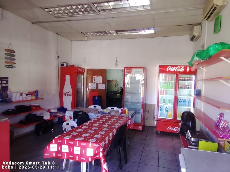 A functional commercial open-plan space featuring tiled flooring, suspended ceiling, and wall-mounted air conditioning, suitable for a small retail or dining establishment.