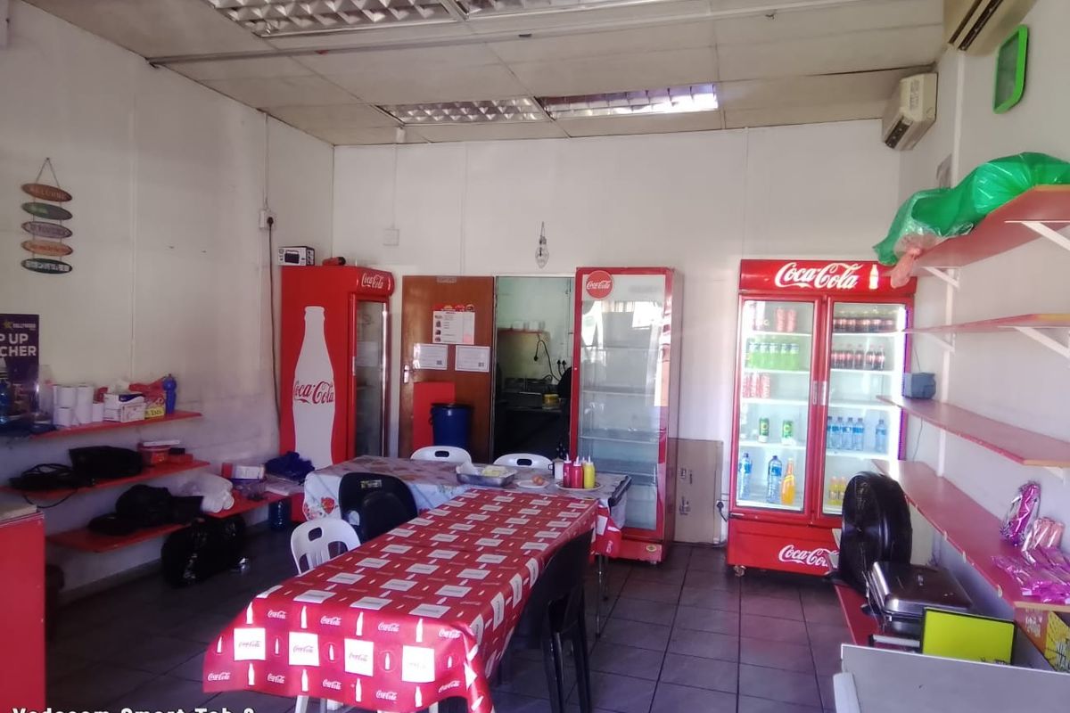 A functional commercial open-plan space featuring tiled flooring, suspended ceiling, and wall-mounted air conditioning, suitable for a small retail or dining establishment.