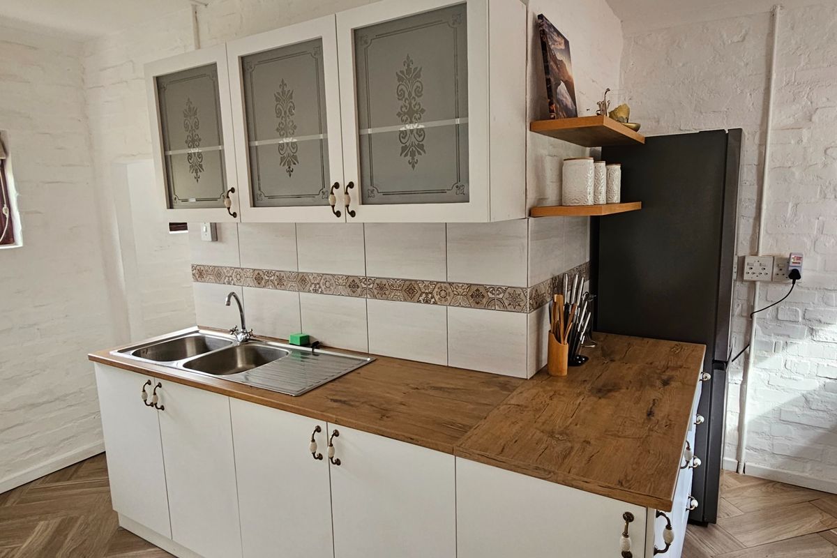 A compact kitchen featuring white cabinetry, wood-look laminate countertops, a stainless steel double sink, and decorative tiled backsplash.