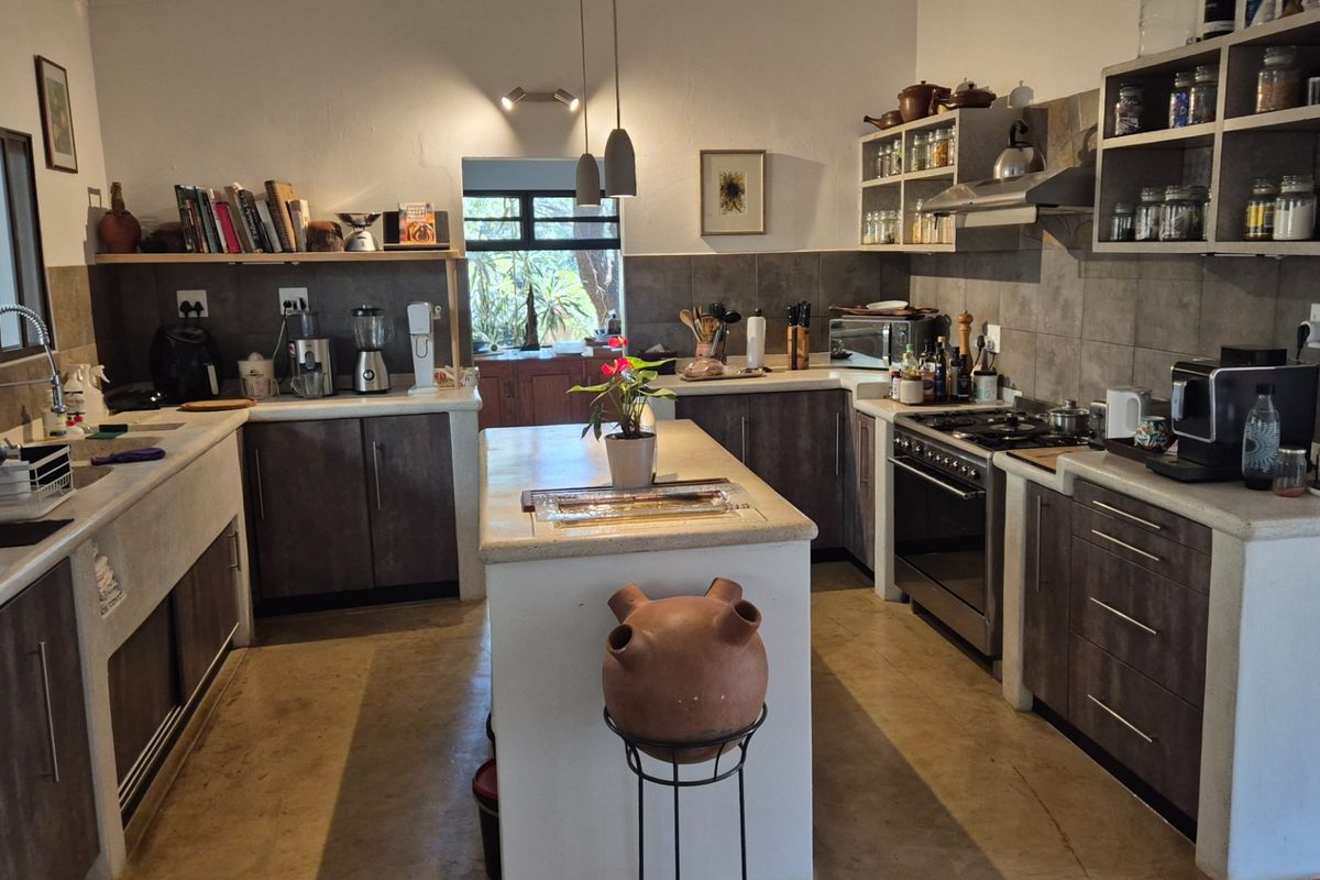 Spacious kitchen featuring a central island, stone-look countertops, dark cabinetry, stainless steel gas stove, and tiled backsplash with ample open shelving.