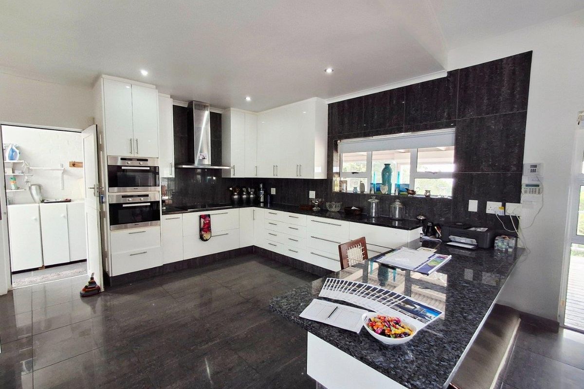 Modern kitchen featuring high-gloss white cabinetry, dark granite countertops, built-in double ovens, stainless steel extractor fan, and a spacious breakfast bar island.