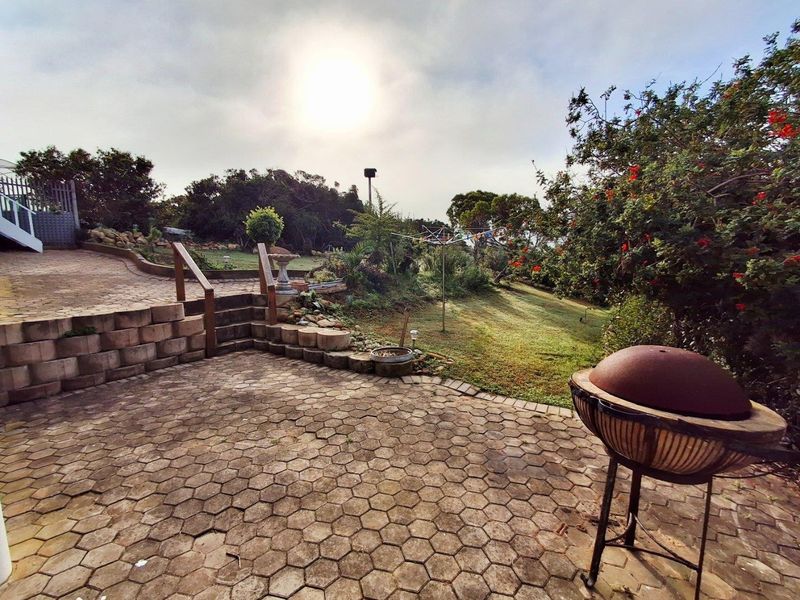 A spacious outdoor patio area featuring hexagonal paving, tiered retaining walls, and a landscaped garden with established greenery.