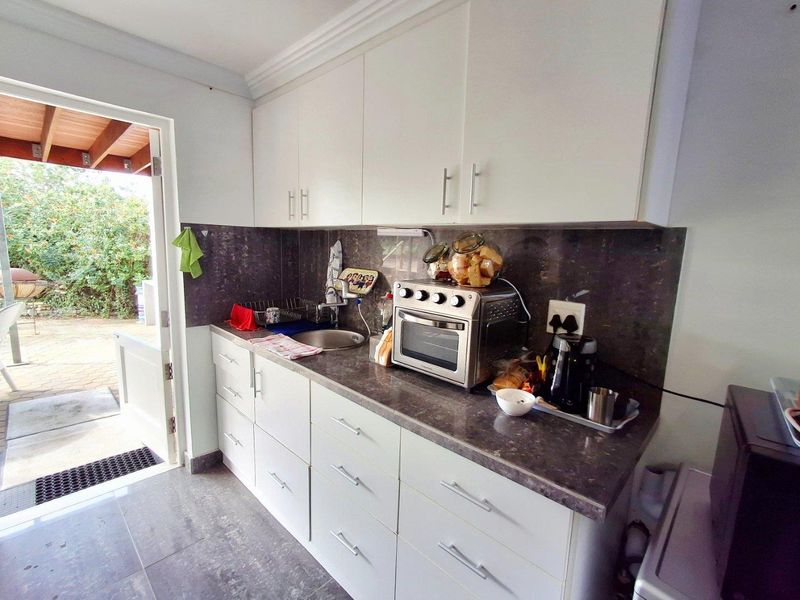 Compact scullery area featuring white cabinetry, dark stone-look countertops, a stainless steel sink, and direct access to an outdoor patio.