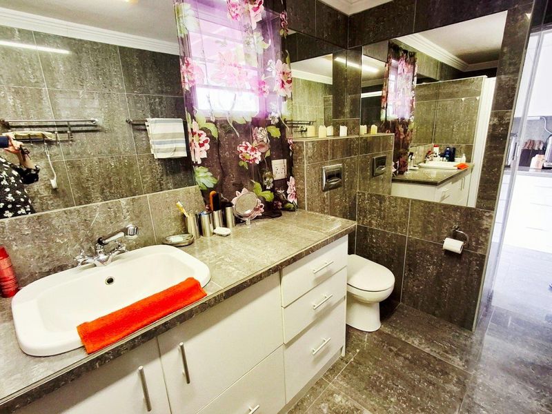 A modern bathroom featuring dark stone-look wall and floor tiles, a white vanity with integrated basin, and a wall-mounted toilet.