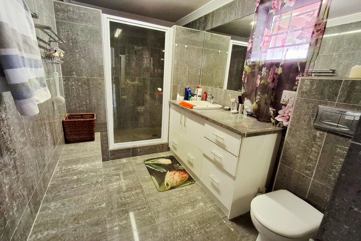 A modern bathroom featuring floor-to-ceiling grey tiling, a built-in vanity with a basin, a glass-enclosed shower, and a wall-mounted toilet.