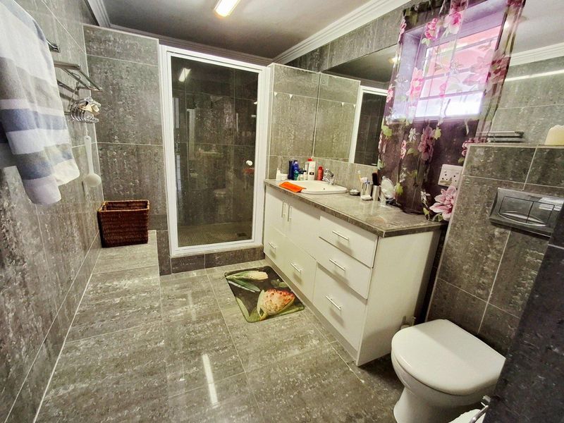 A modern bathroom featuring floor-to-ceiling grey tiling, a built-in vanity with a basin, a glass-enclosed shower, and a wall-mounted toilet.
