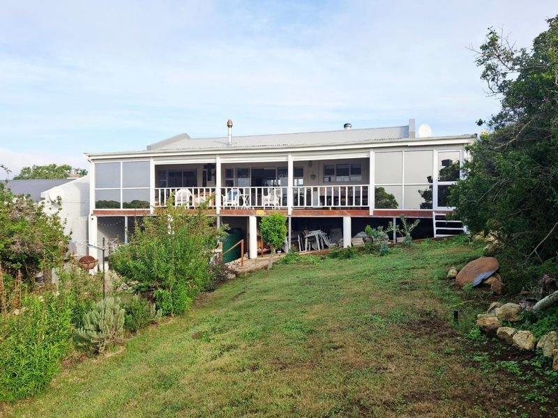 Rear view of the property featuring an elevated covered deck with glass enclosures, overlooking a sloped garden area.