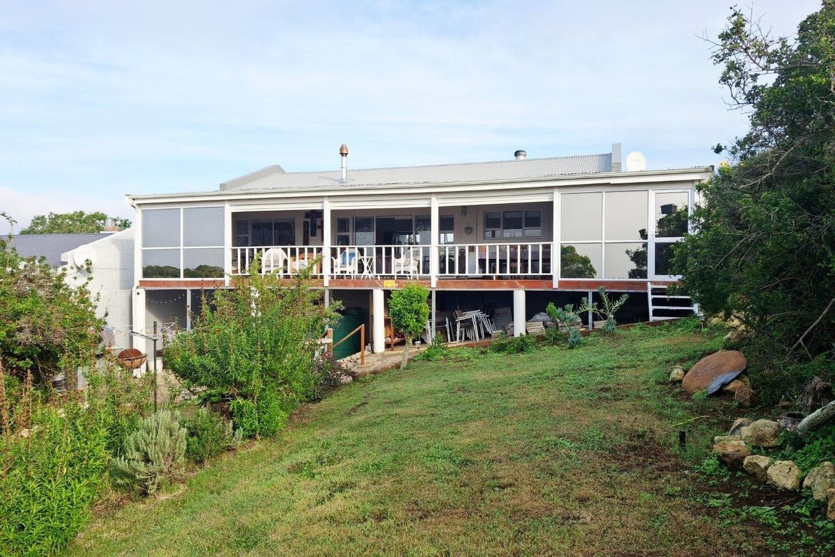 Rear view of the property featuring an elevated covered deck with glass enclosures, overlooking a sloped garden area.