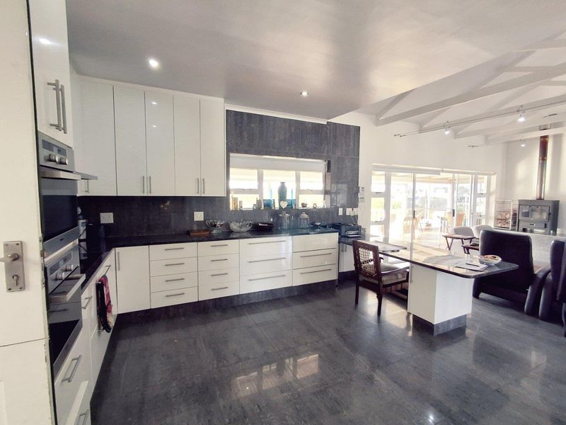 Modern open-plan kitchen featuring high-gloss cabinetry, dark stone countertops, built-in oven, and seamless flow into the adjacent living area with vaulted ceilings.