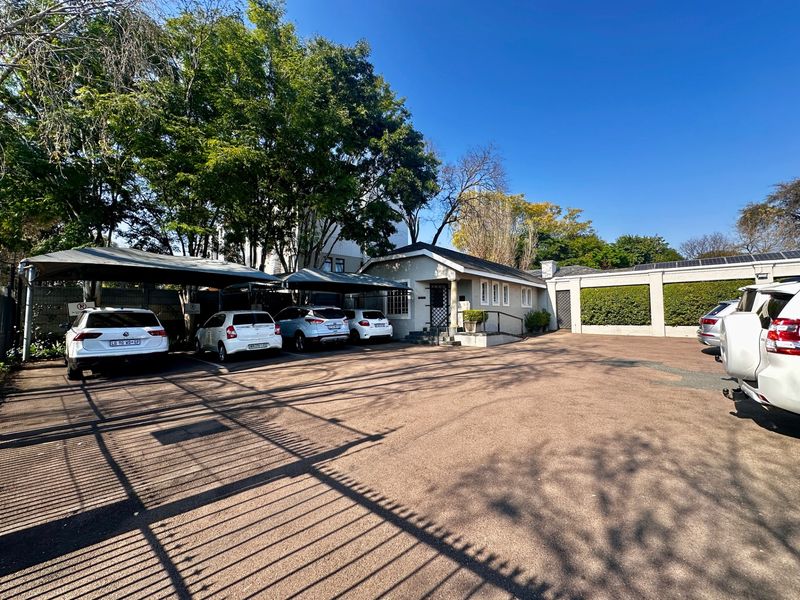 Exterior view of the property entrance featuring a paved driveway, covered parking bays, and established garden landscaping.
