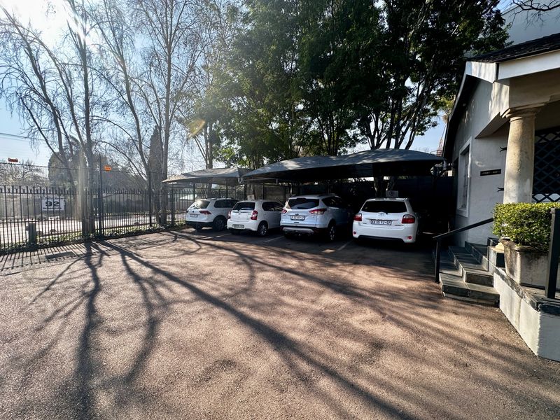 Exterior view of the property featuring a paved driveway with covered parking bays and mature trees.