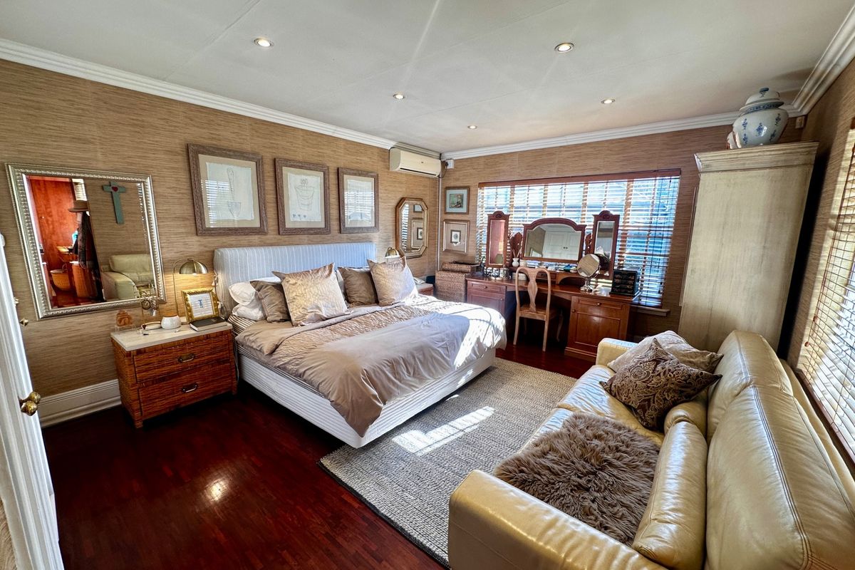 Spacious bedroom featuring warm-toned textured wallpaper, polished hardwood flooring, recessed ceiling lighting, and a wall-mounted air conditioning unit.