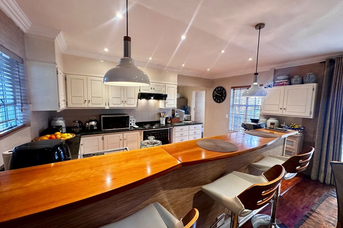 A well-appointed kitchen featuring a raised wooden breakfast bar, white cabinetry, dark countertops, and integrated lighting, creating a functional and inviting culinary space.