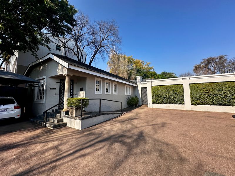 Front exterior view of the property featuring a paved driveway, covered entrance with stone steps, and a perimeter wall with integrated hedging.
