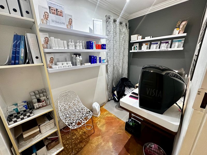 A compact utility or treatment room featuring built-in shelving, a desk area, and professional aesthetic equipment.