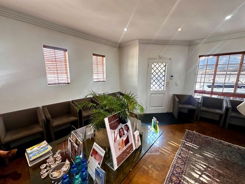 A bright reception or waiting area featuring tiled flooring, recessed ceiling lighting, and multiple windows with fitted blinds.