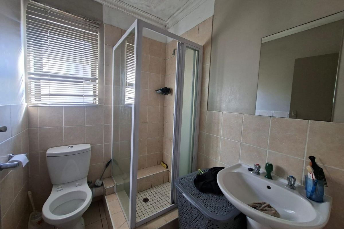 A functional bathroom featuring a glass-enclosed shower, pedestal basin, wall-mounted mirror, and toilet with neutral wall tiling.