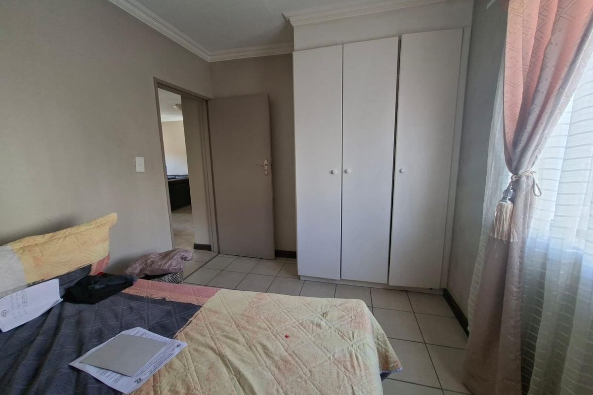A bedroom featuring built-in white cabinetry, tiled flooring, and a window with curtain treatments.