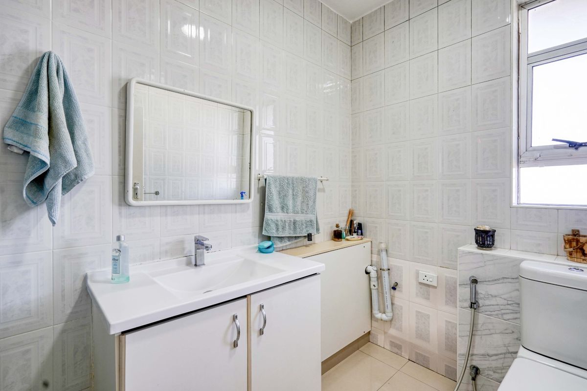 A functional bathroom featuring a vanity cabinet, wall-mounted mirror, toilet with bidet spray, and full-height wall tiling.