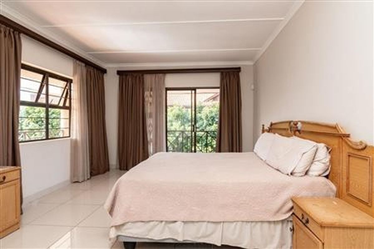 Spacious bedroom featuring tiled flooring, large windows with security bars, and sliding door access to a private balcony.